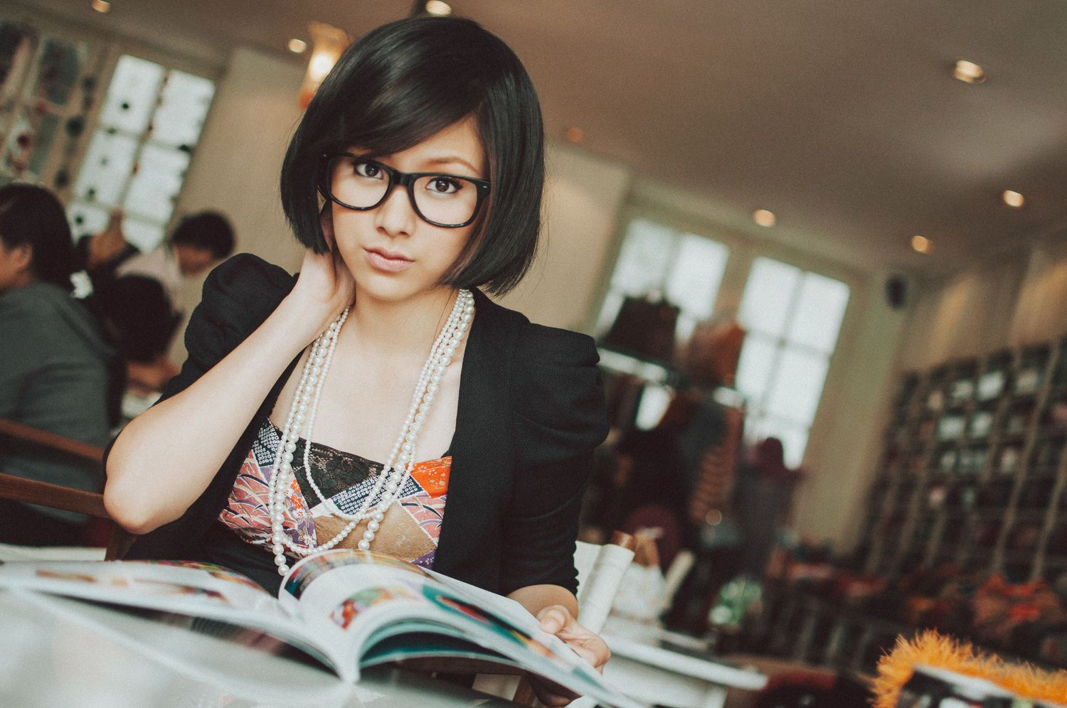 Student wearing glasses studies from textbook in library setting.