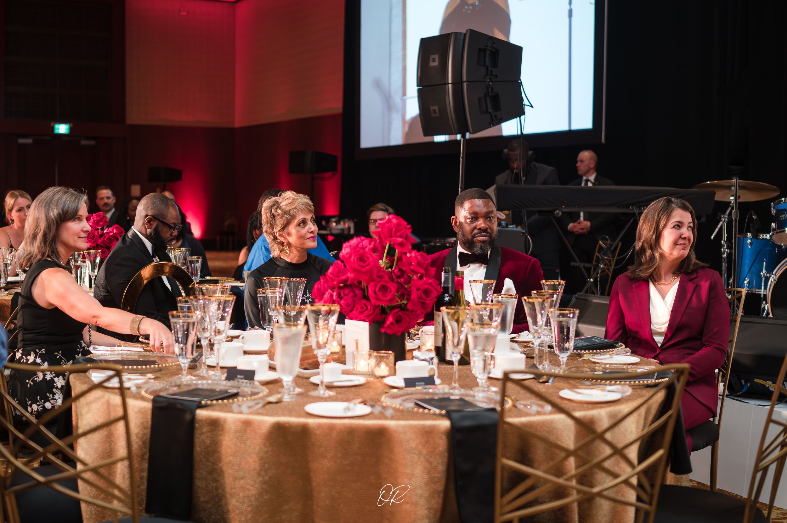 Guests seated at an elegant round table with pink floral centerpieces at a formal evening event.