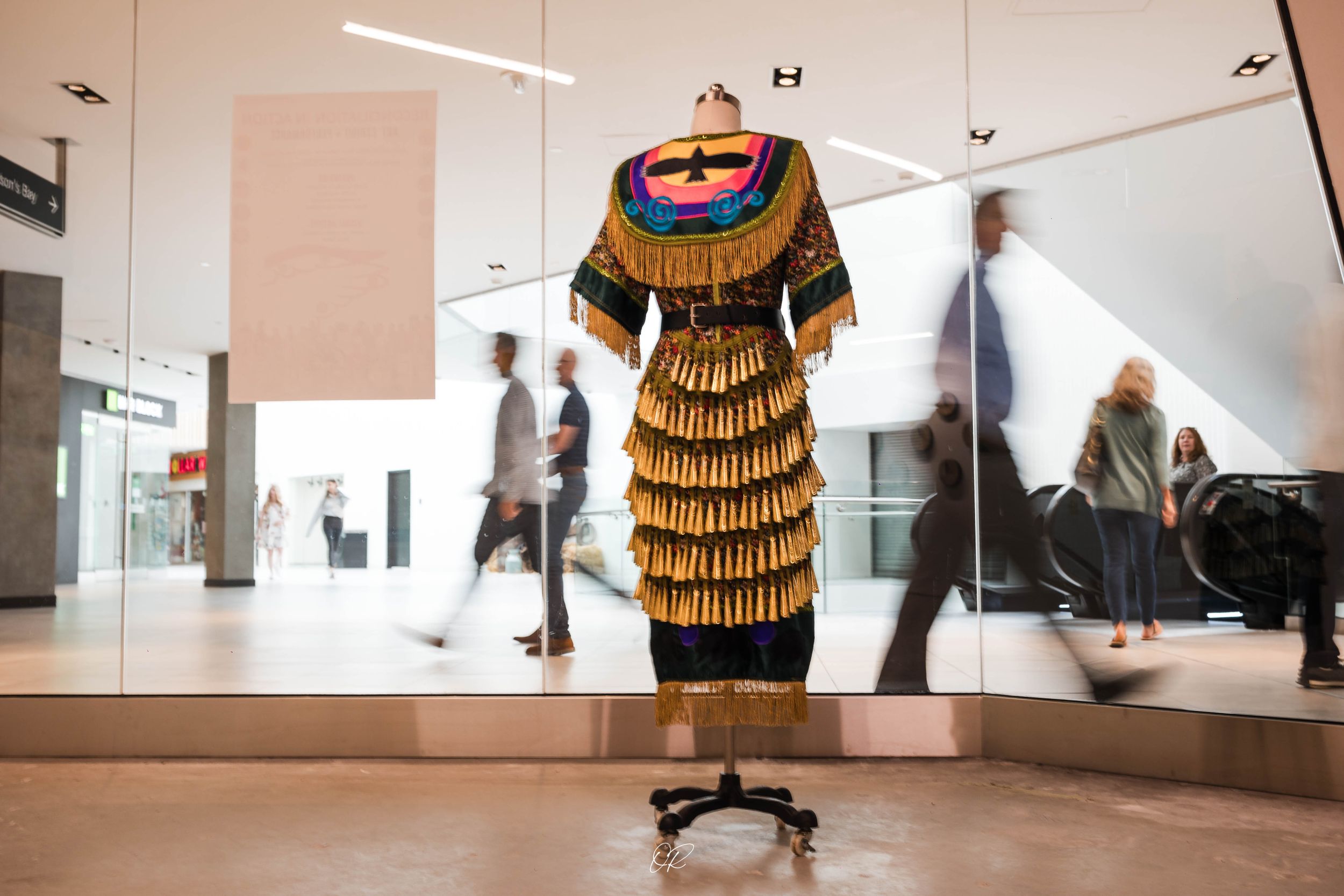 Traditional Native American dress with gold fringe tiers displayed on mannequin in modern retail setting.