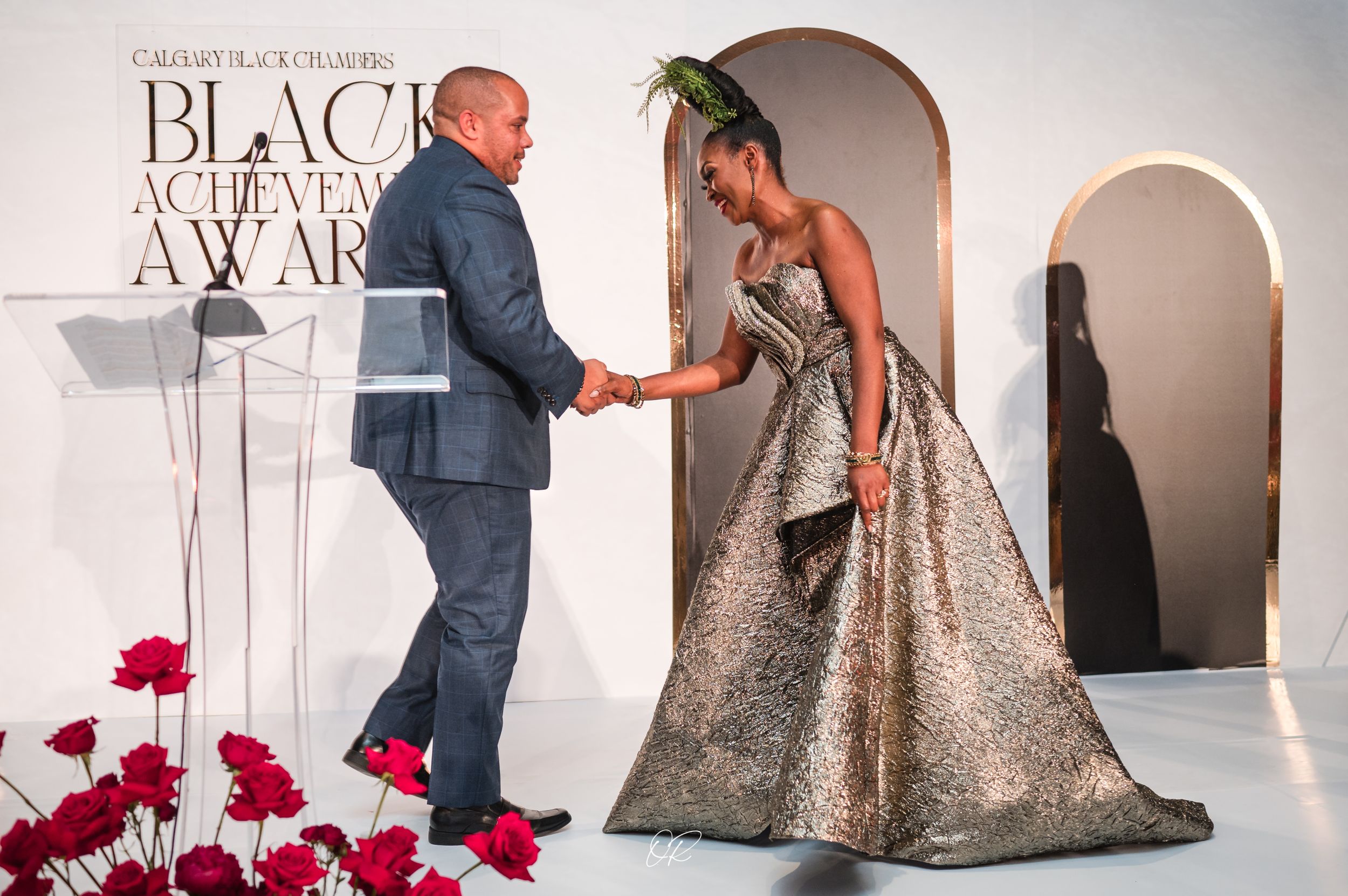 A stunning metallic gown with a dramatic silhouette at an awards ceremony with red floral decorations.