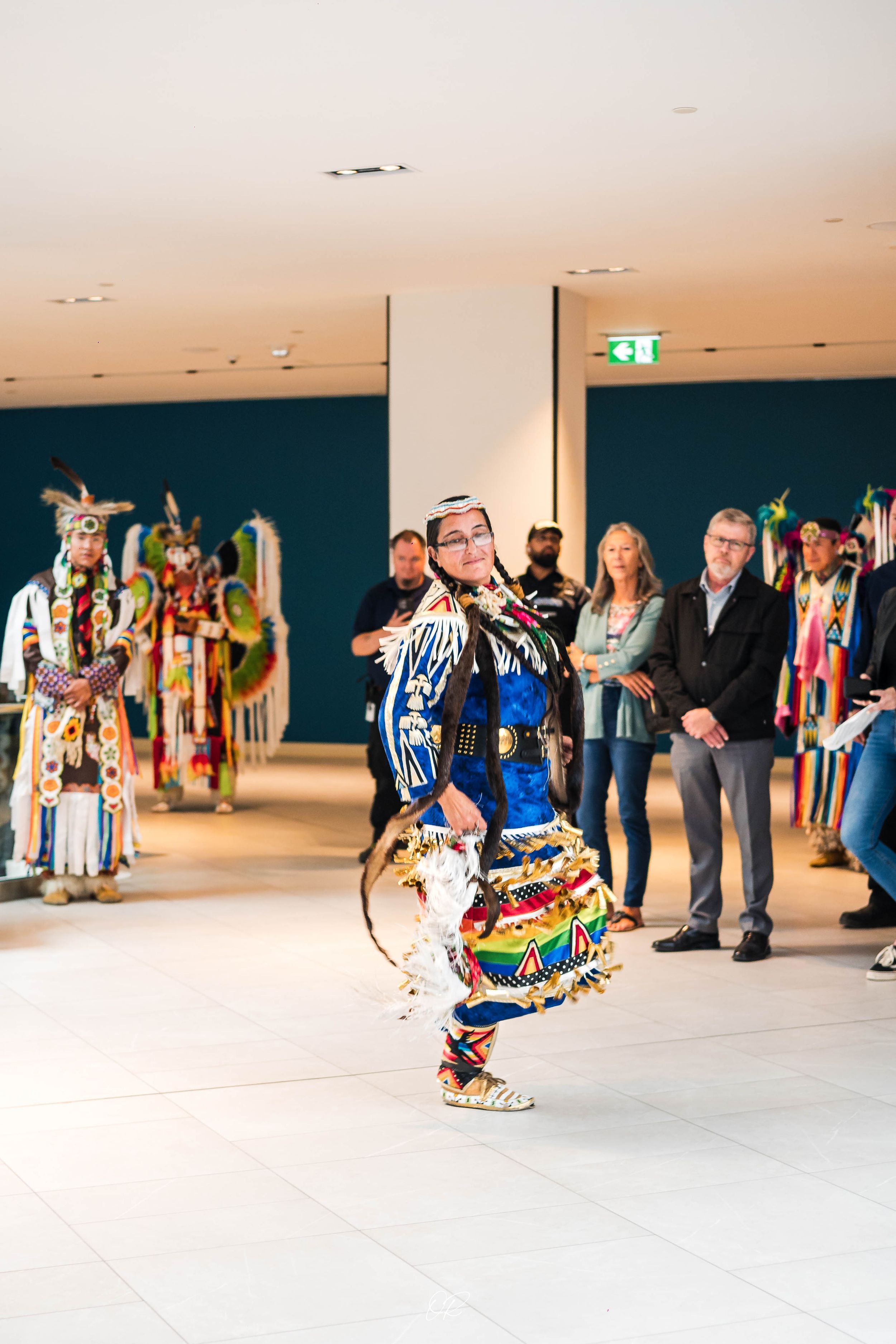 Native American dancers perform traditional dances in colorful regalia while spectators watch from the sidelines.