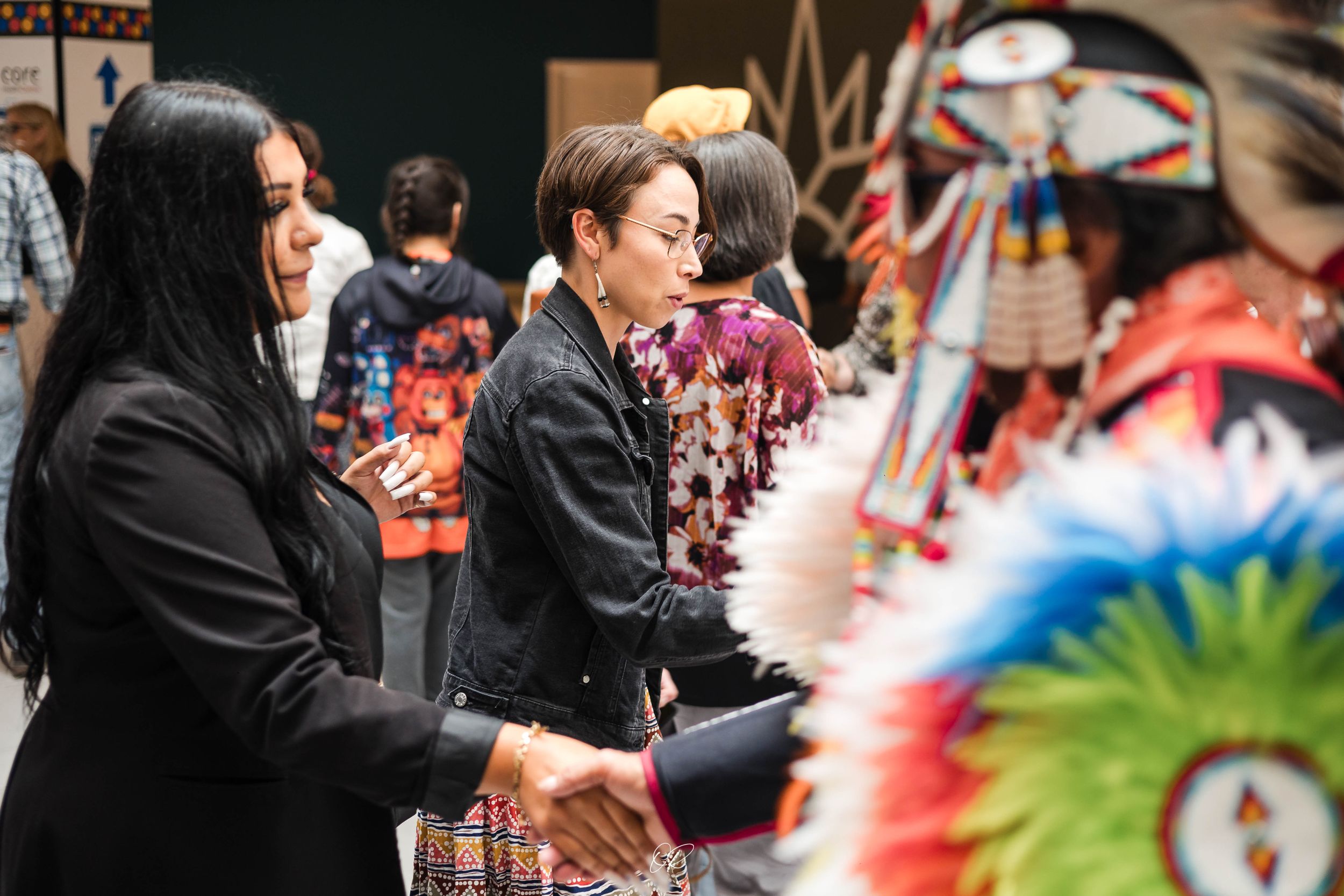 Spectators watch a colorful traditional Native American powwow dance performance with vibrant feathered regalia.