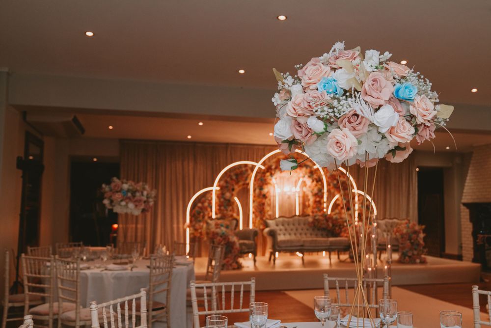 Romantic wedding table centerpiece with pink and blue flowers under an illuminated floral arch.