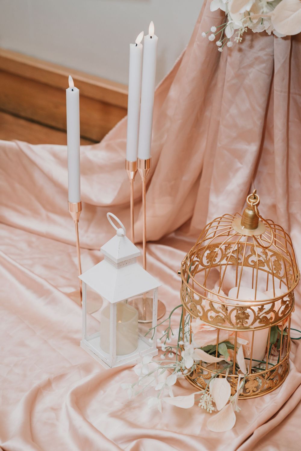 Romantic wedding decor featuring white lanterns and gold birdcage on blush pink fabric.