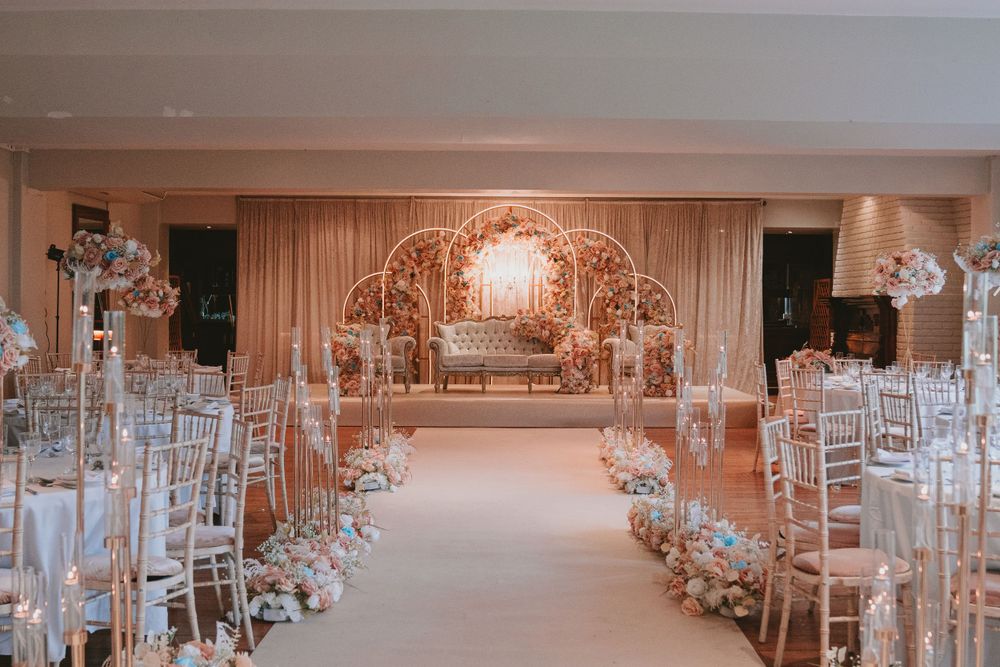 Wedding ceremony aisle with gold arch backdrop and white chiavari chairs lined with floral arrangements.