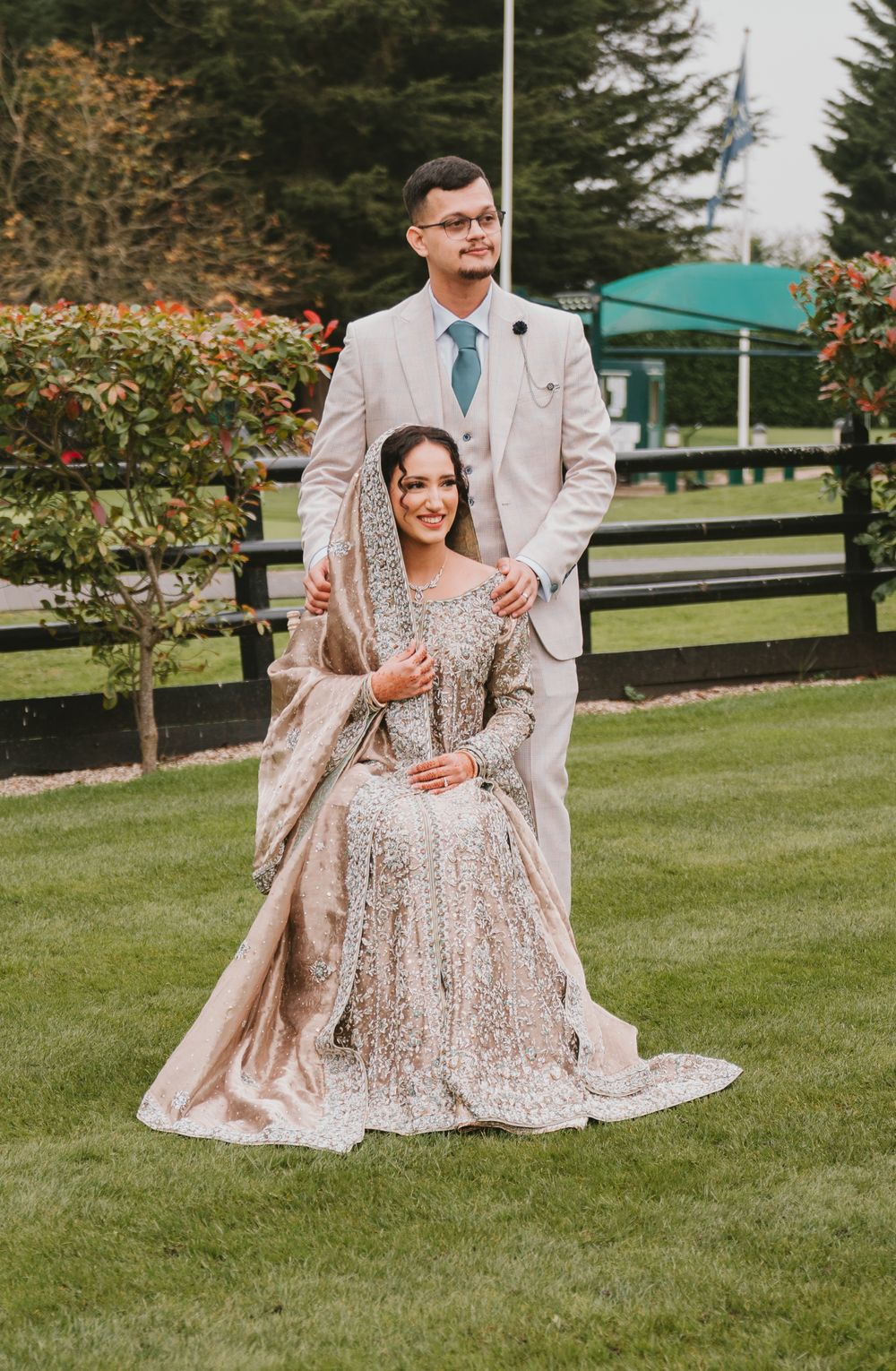 Wedding couple outdoors in coordinated light-colored formal attire on grassy lawn.