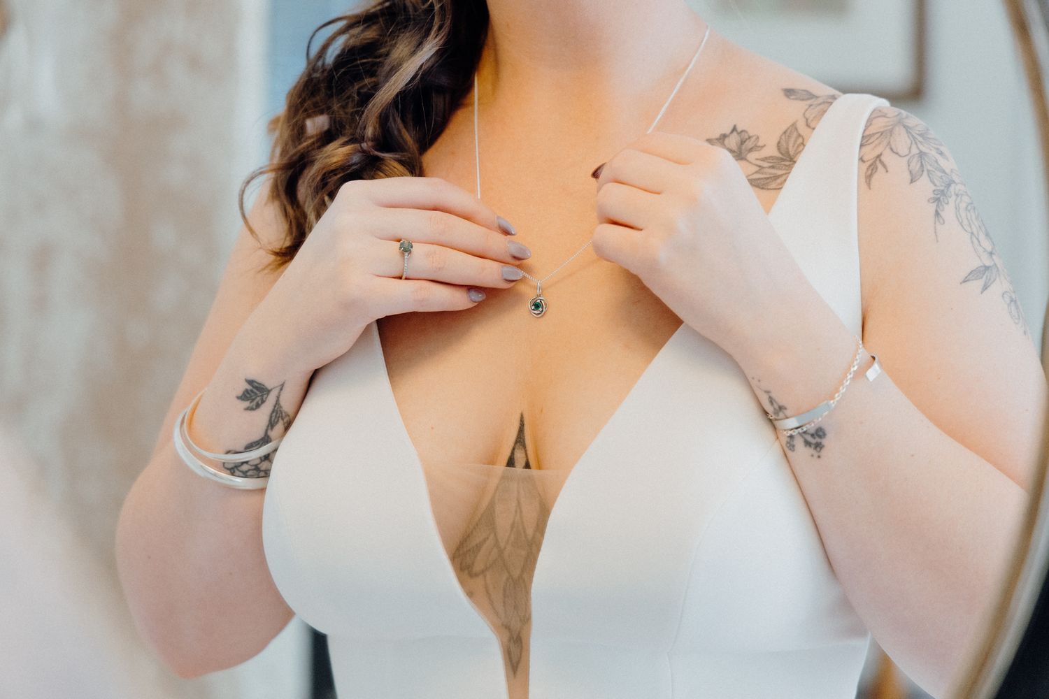 Bride close-up shot with delicate tattoos adjusting a white lace bodice top, captured by Apertured Media Auckland Wedding Photographer.