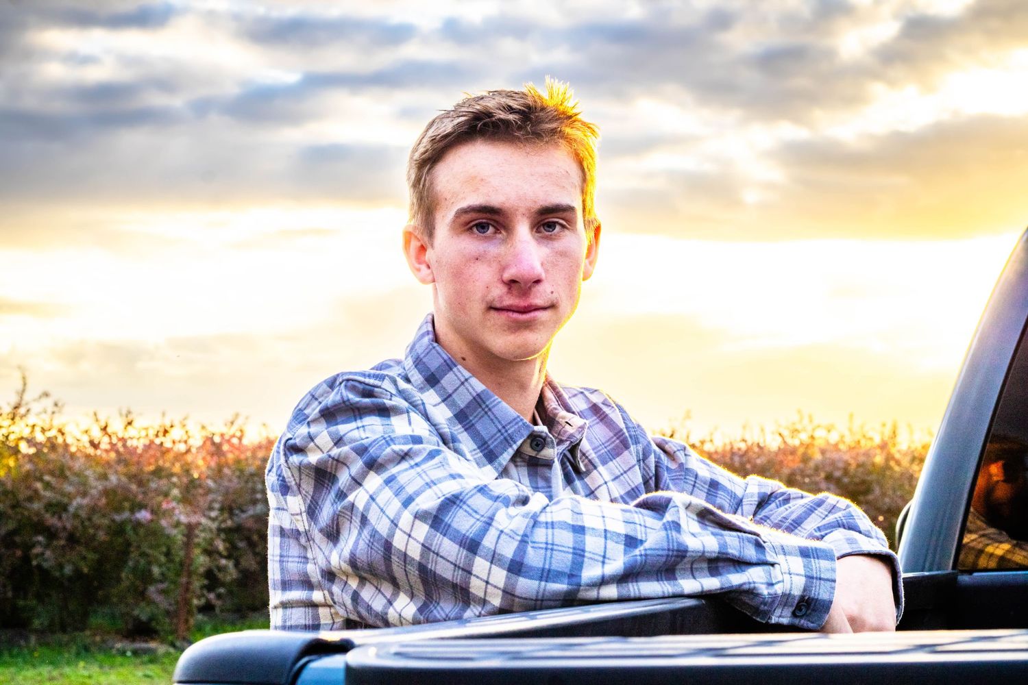 young man leans against truck and looks at the camera as the sun shines over his shoulder