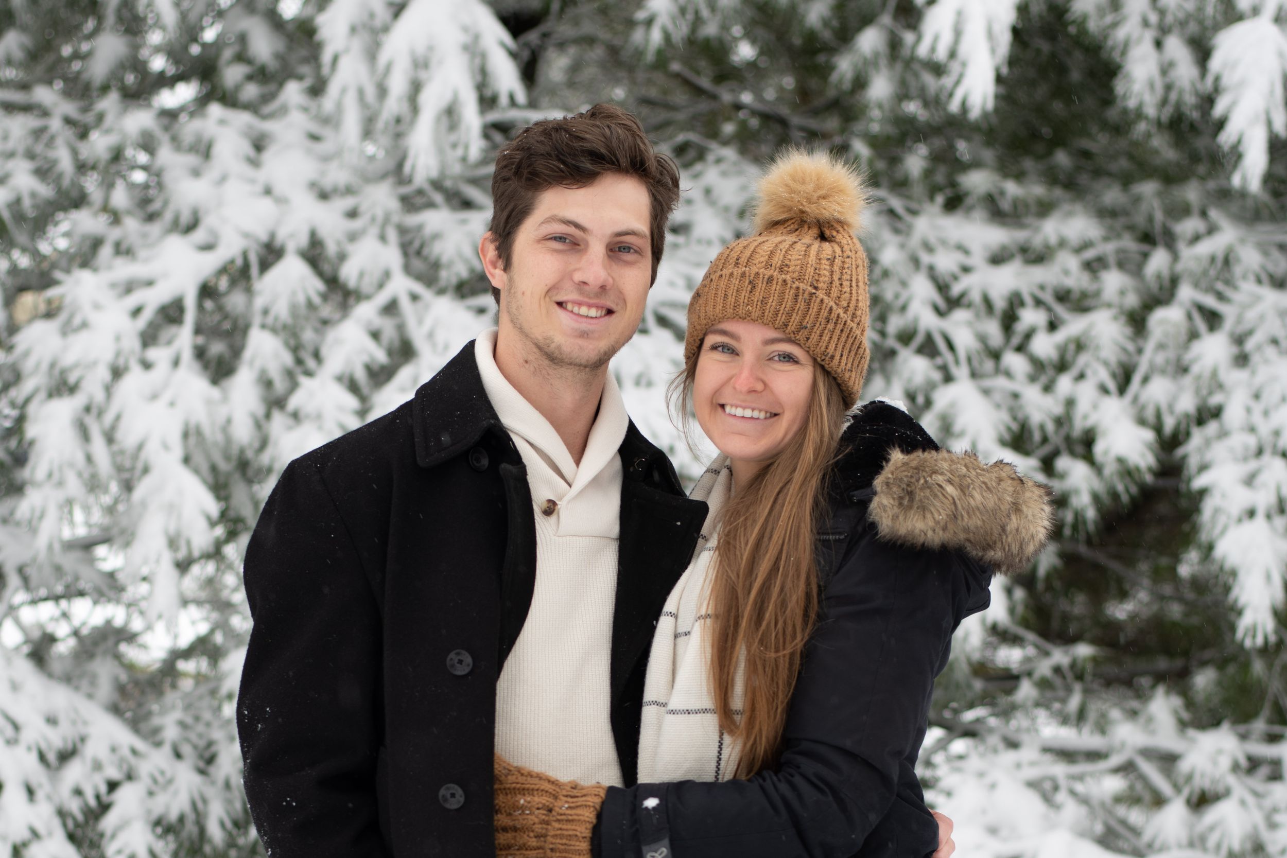 A winter portrait featuring two people in coordinated outfits against snowy evergreens.