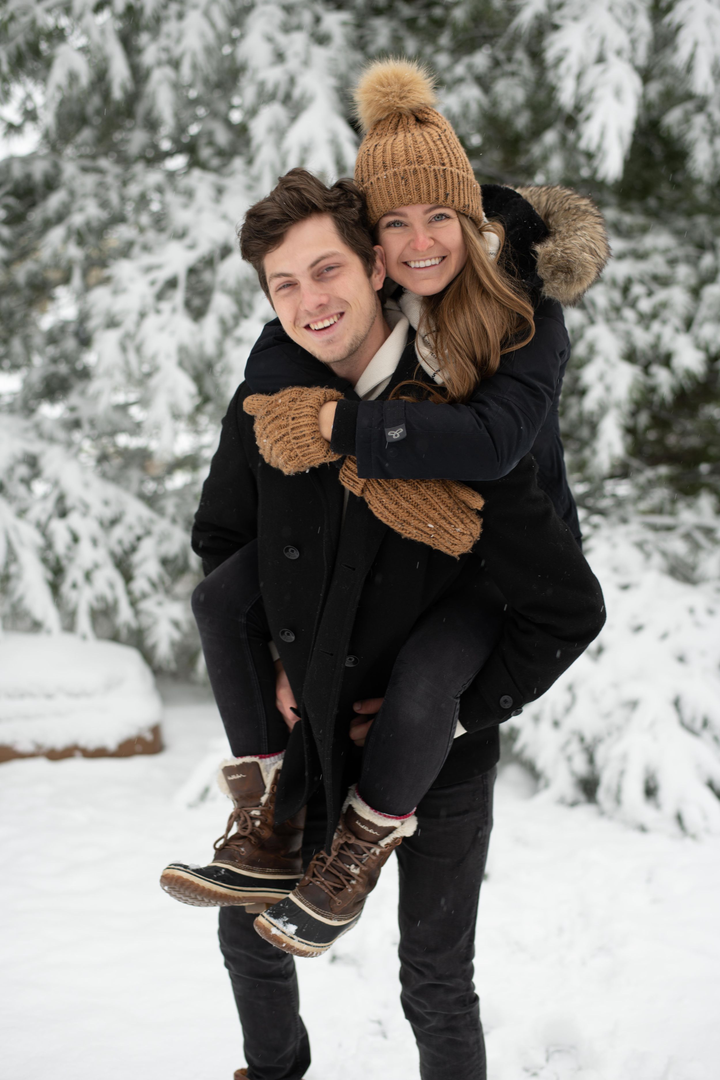 A joyful winter moment with matching tan winter accessories against a snowy evergreen backdrop.