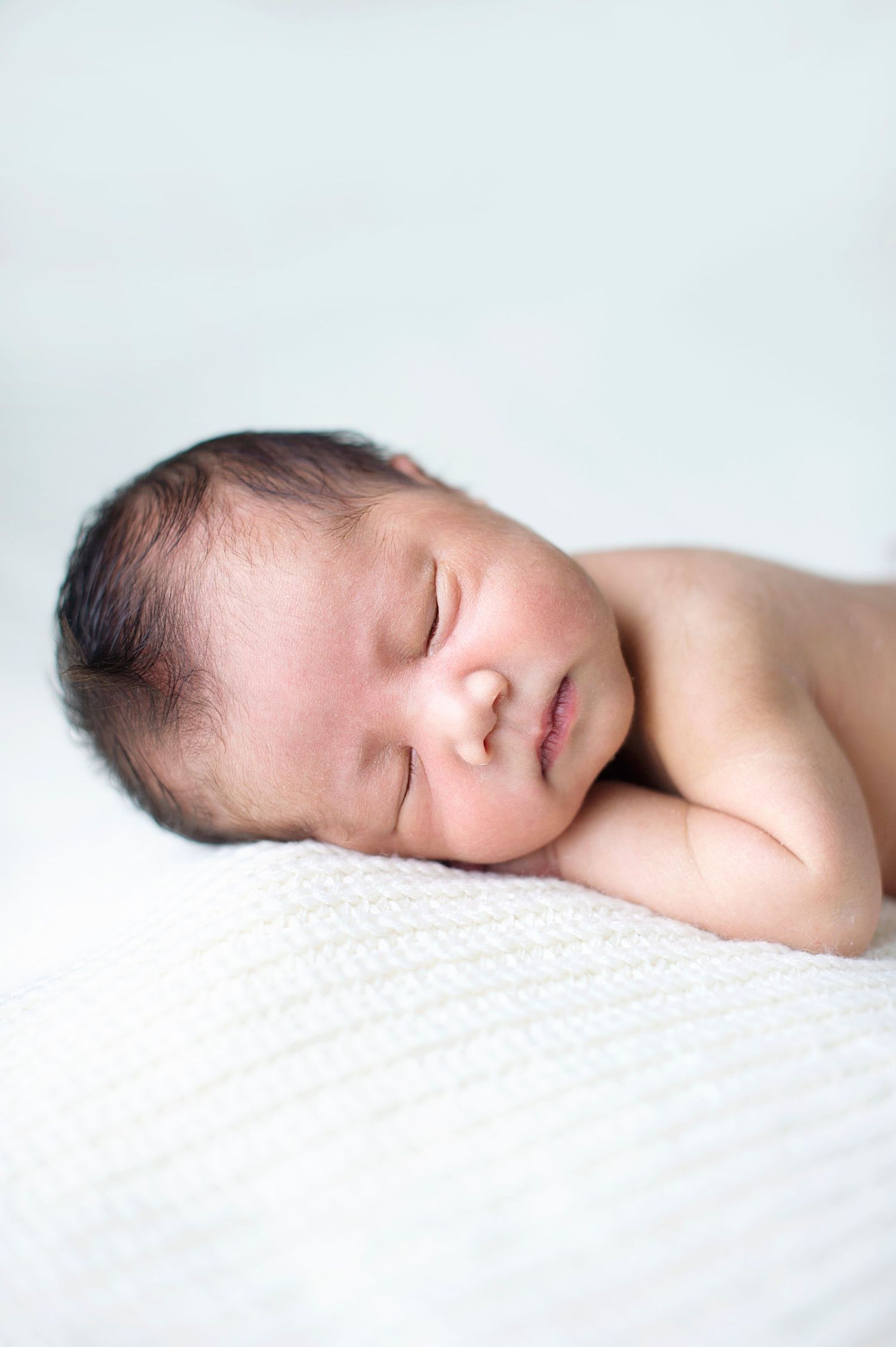 Peaceful newborn boy dozing on a white blanket, photographed by Phoebe Lee Photo in Toronto