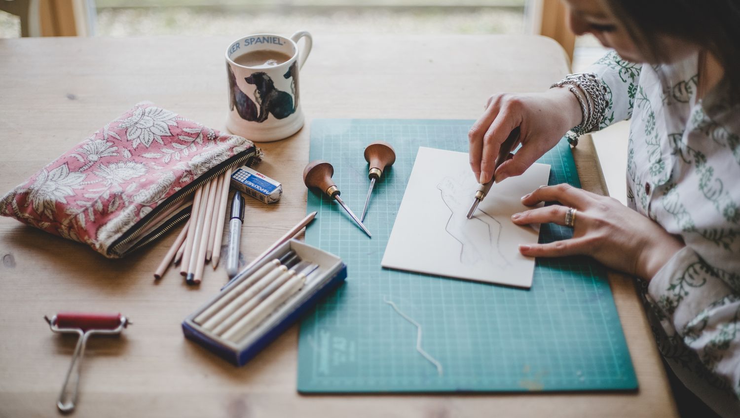 Someone works on a craft project at a desk with photos, pencils and supplies.