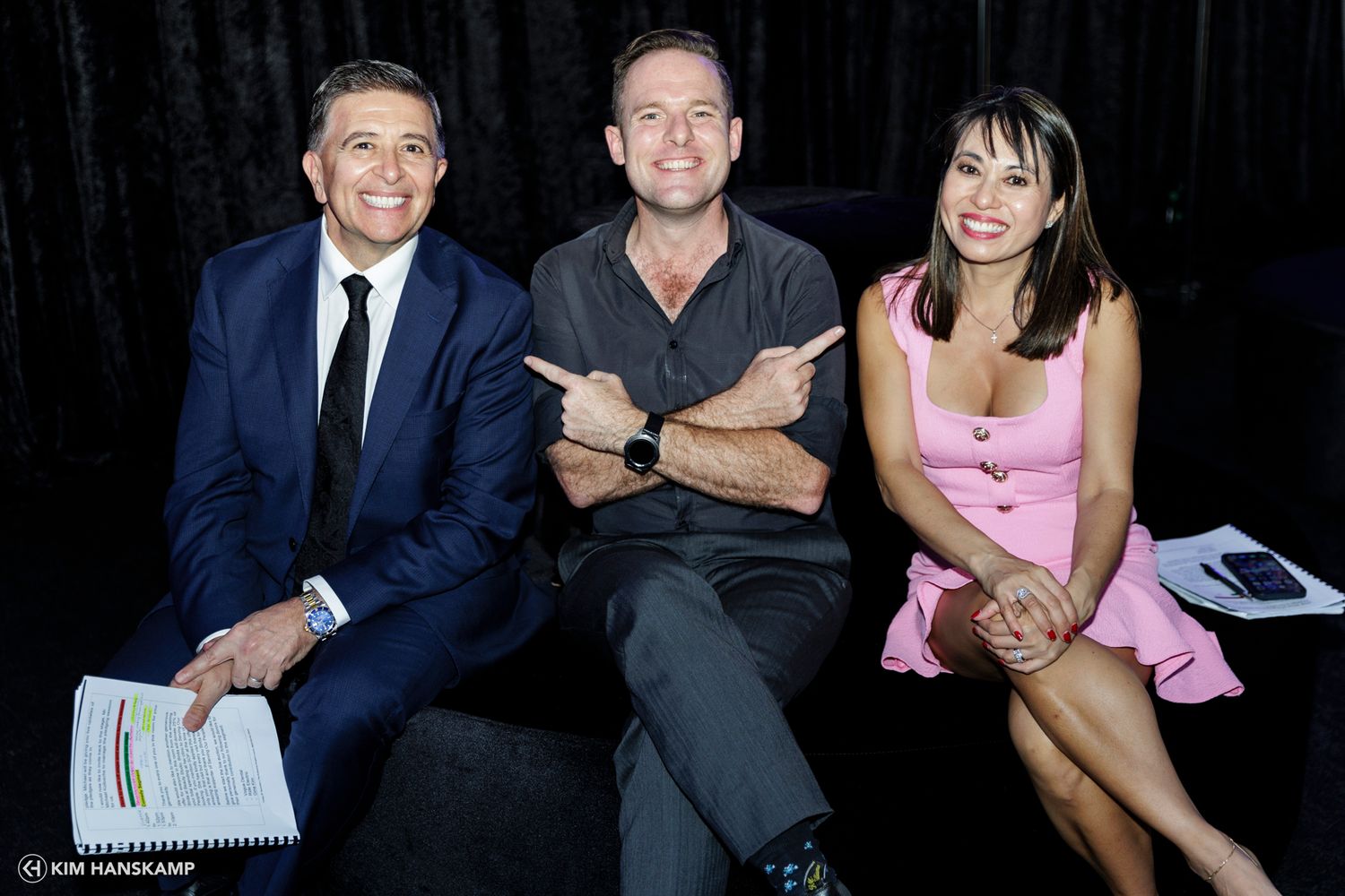 Three people sitting on a black couch during what appears to be a media event or interview setting.