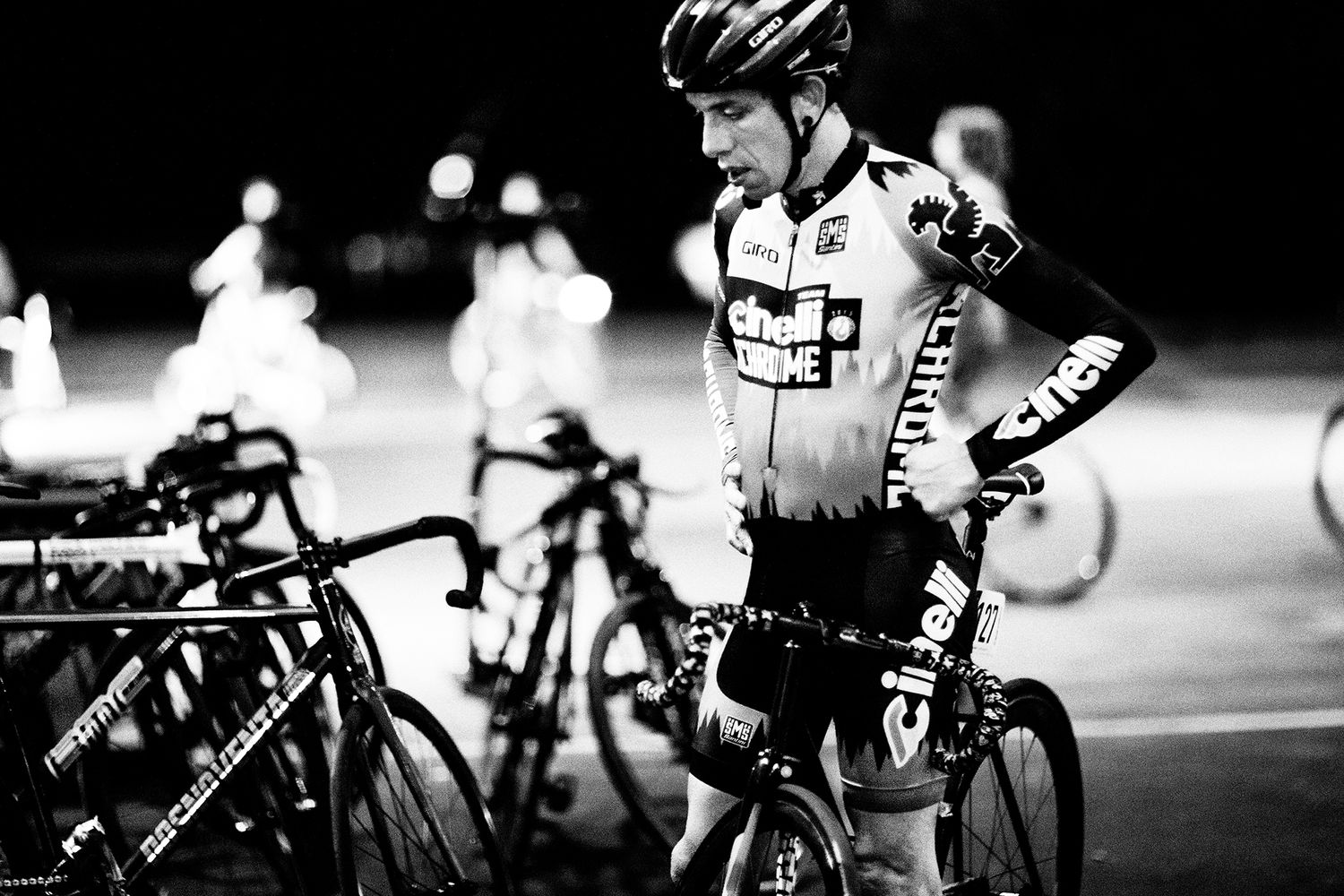 Cyclist in racing gear stands with bike during a nighttime competition.