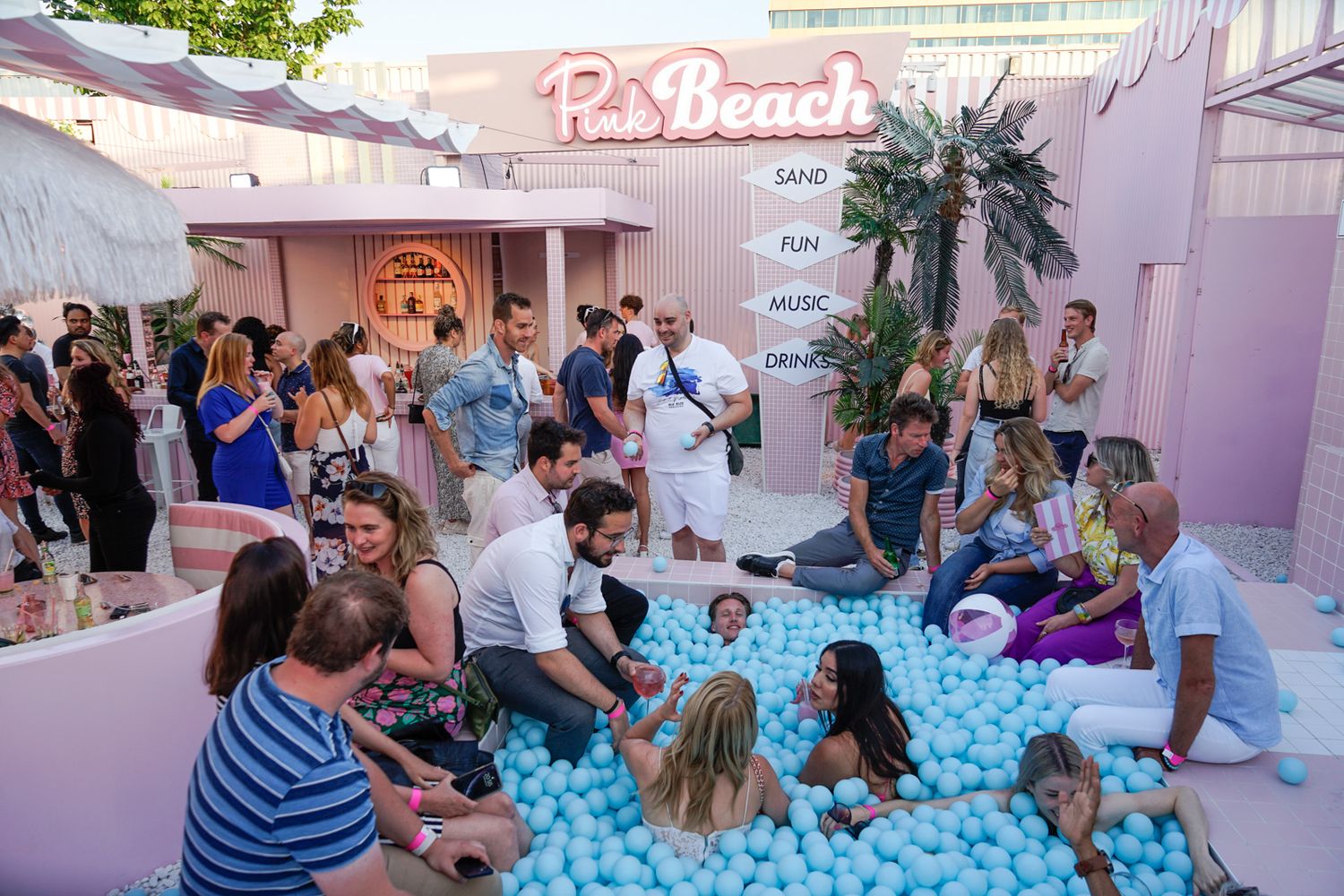 Group of people enjoying a pink-themed social gathering with a white ball pit installation at an event space.
