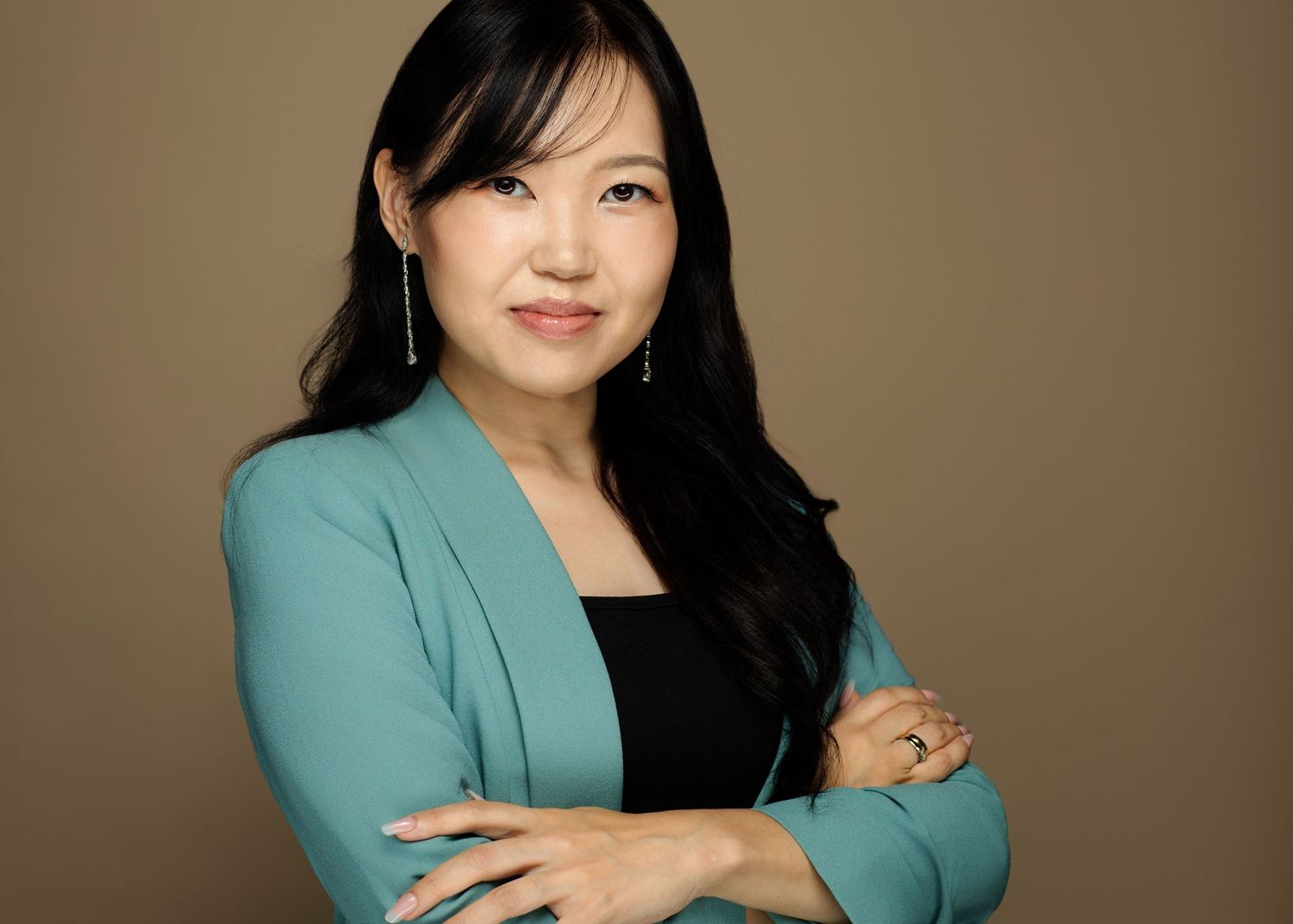 Professional headshot portrait of person in turquoise blazer and black top against neutral brown backdrop.