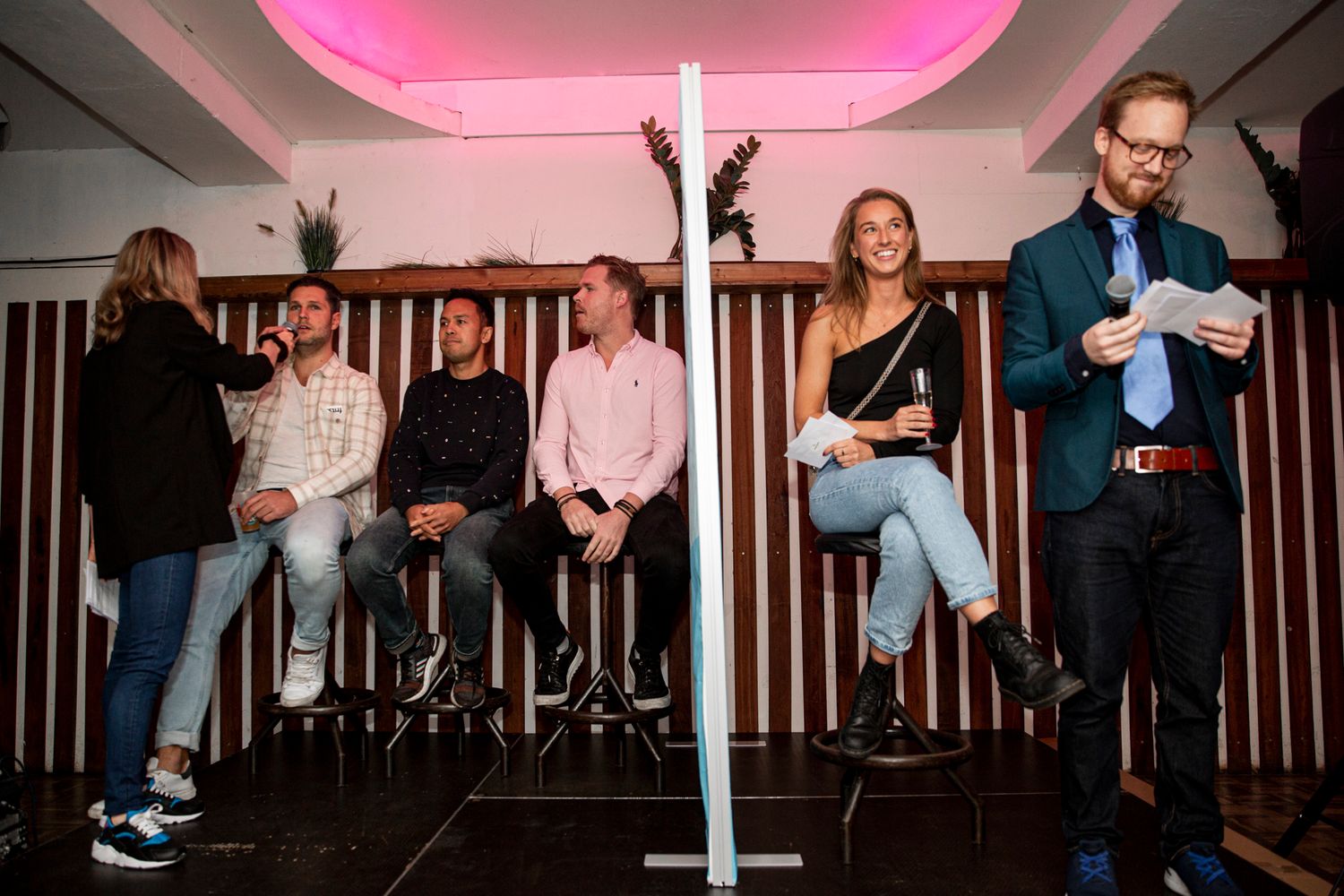 People sitting on bar stools under pink ambient lighting in a modern venue.