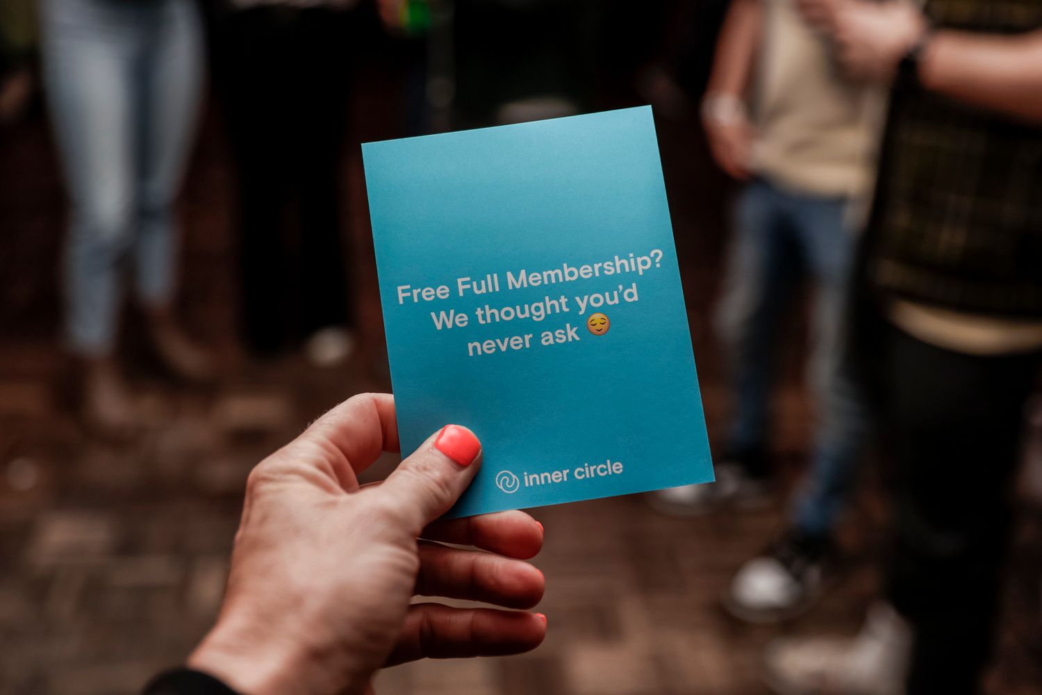 Hand holds a teal colored event membership card against a dark background.