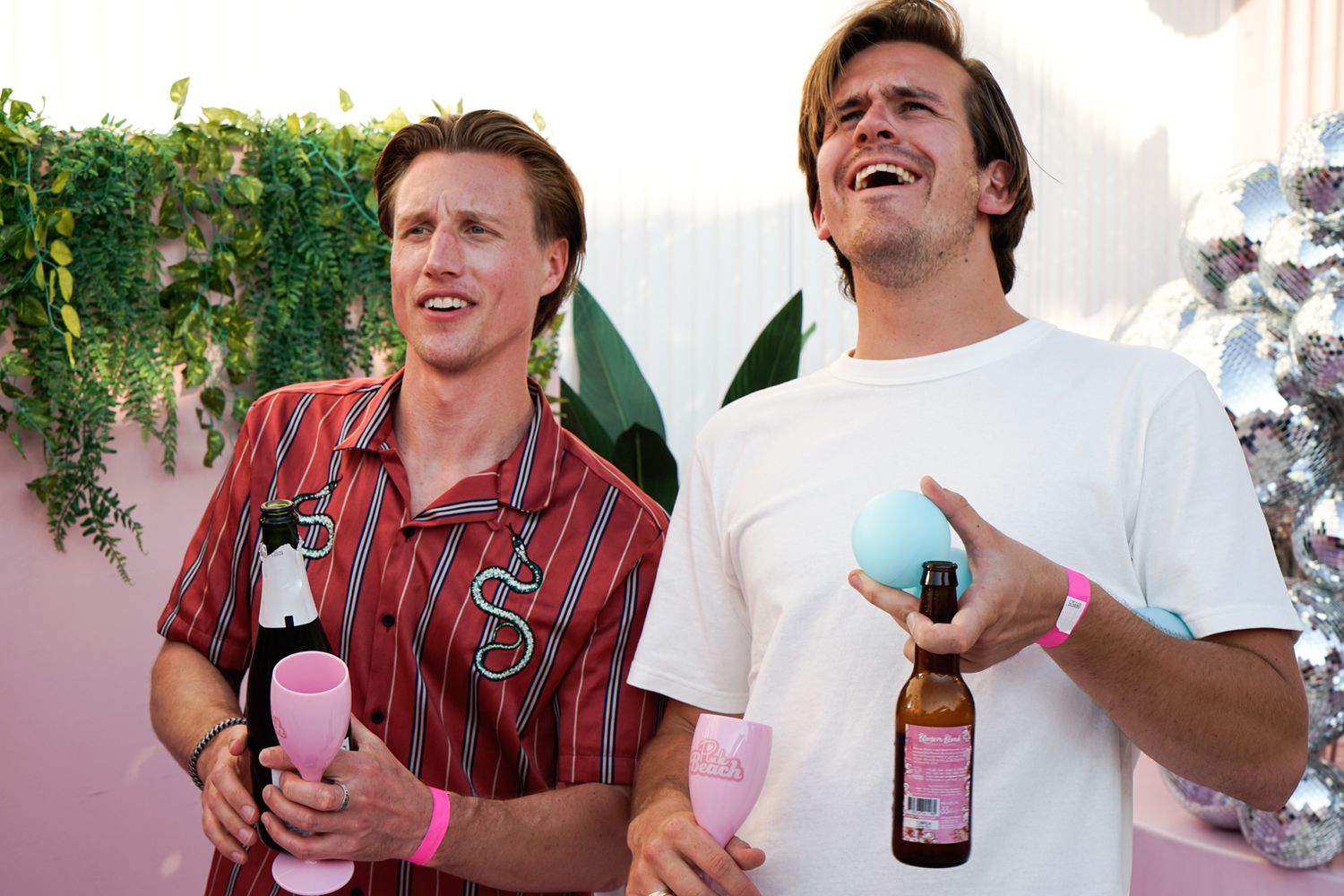 Two friends enjoying drinks outdoors with greenery in background.
