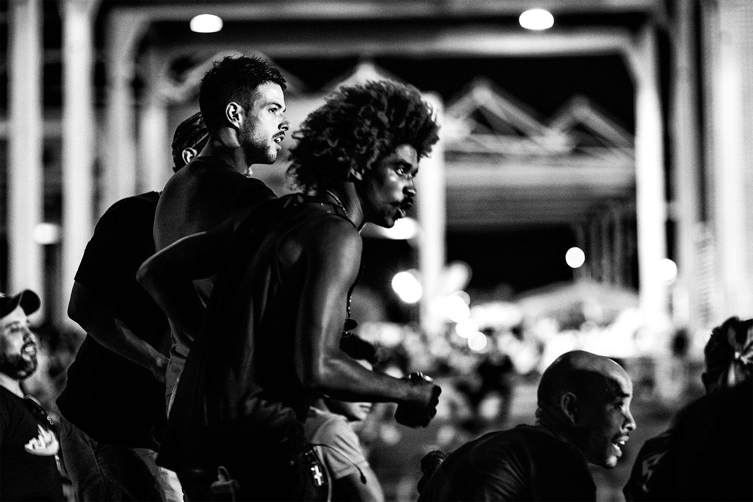 Silhouetted spectators watch intently during a nighttime cycling event.