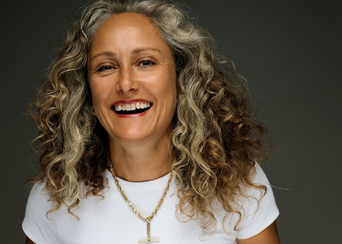 Candid portrait showing joyful expression with natural curly blonde hair wearing white t-shirt and gold necklace.