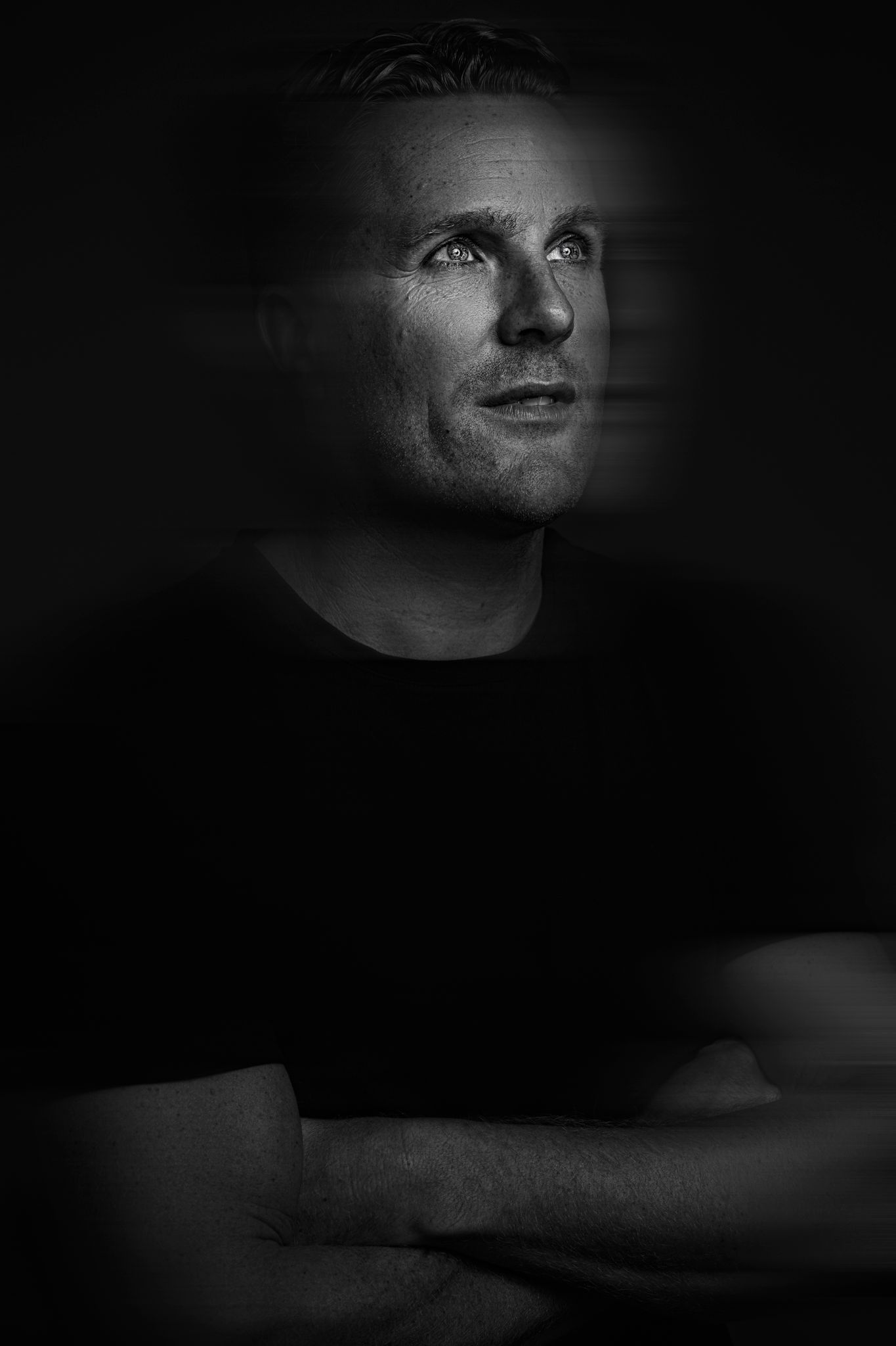 Moody black and white portrait with dramatic lighting against dark background.