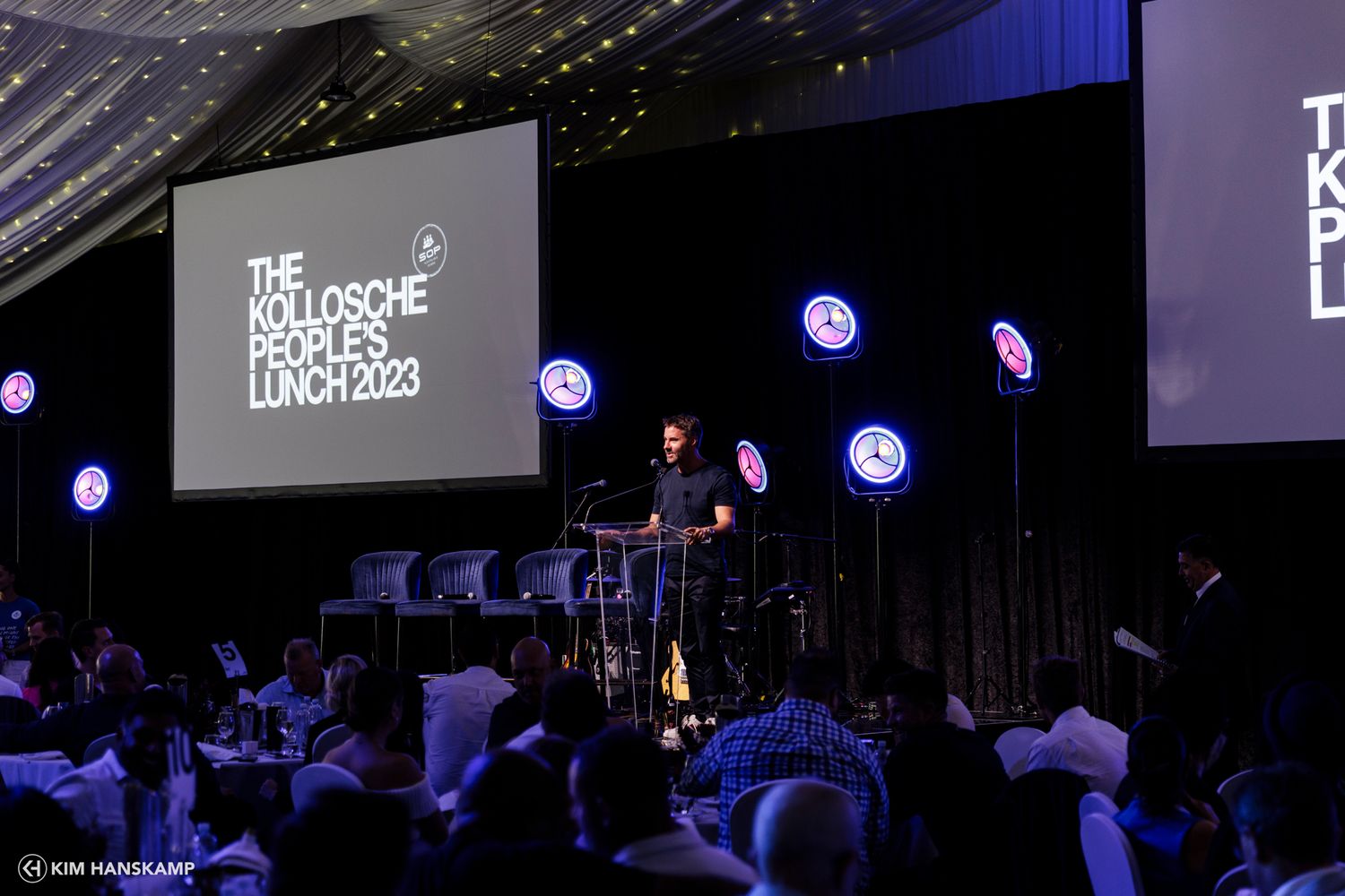 Dark venue with stage lighting and presentation screen during corporate event.