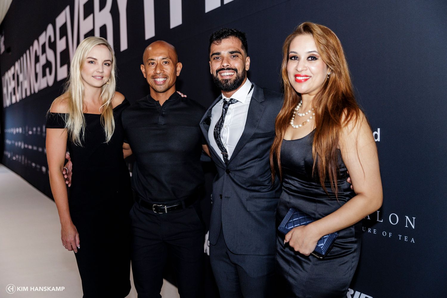 Four people in formal attire posed against black backdrop at elegant event.