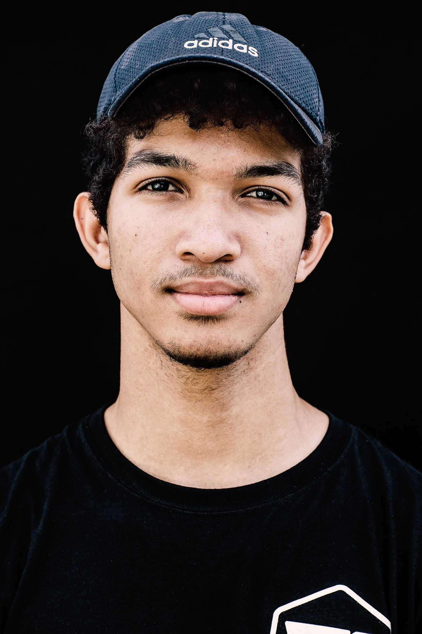 Portrait of someone wearing an Adidas cap against a dark background.