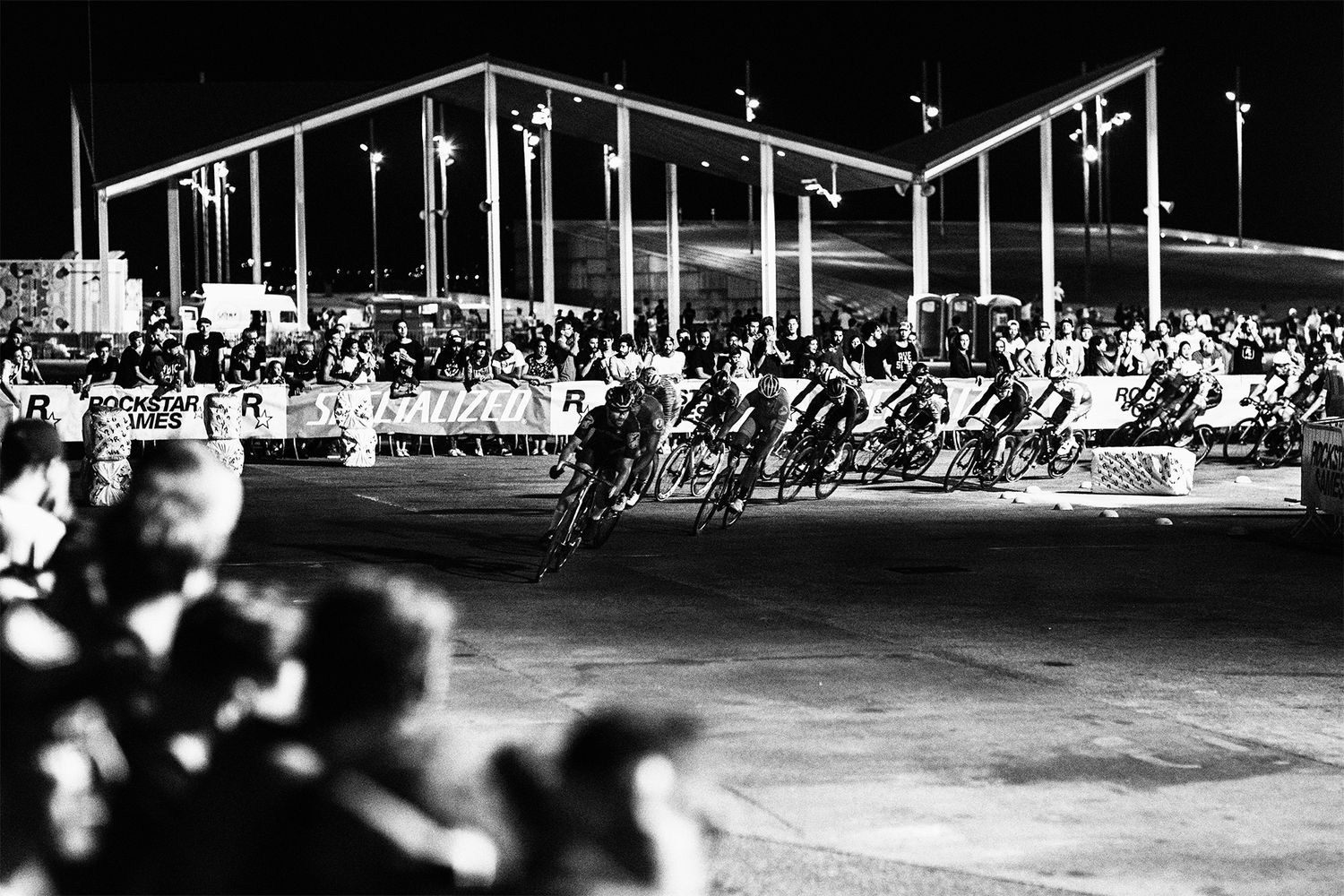 Black and white shot of cyclists racing on a velodrome track with spectators watching.