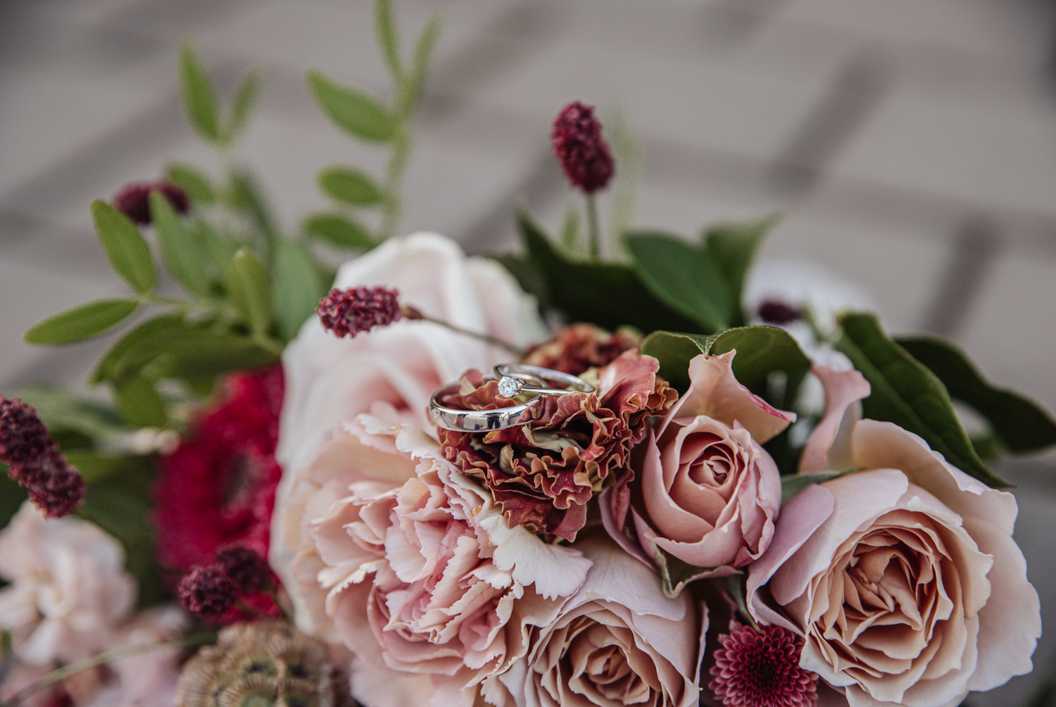 A romantic bouquet featuring blush pink roses, dark burgundy accents, and delicate green foliage in soft focus.