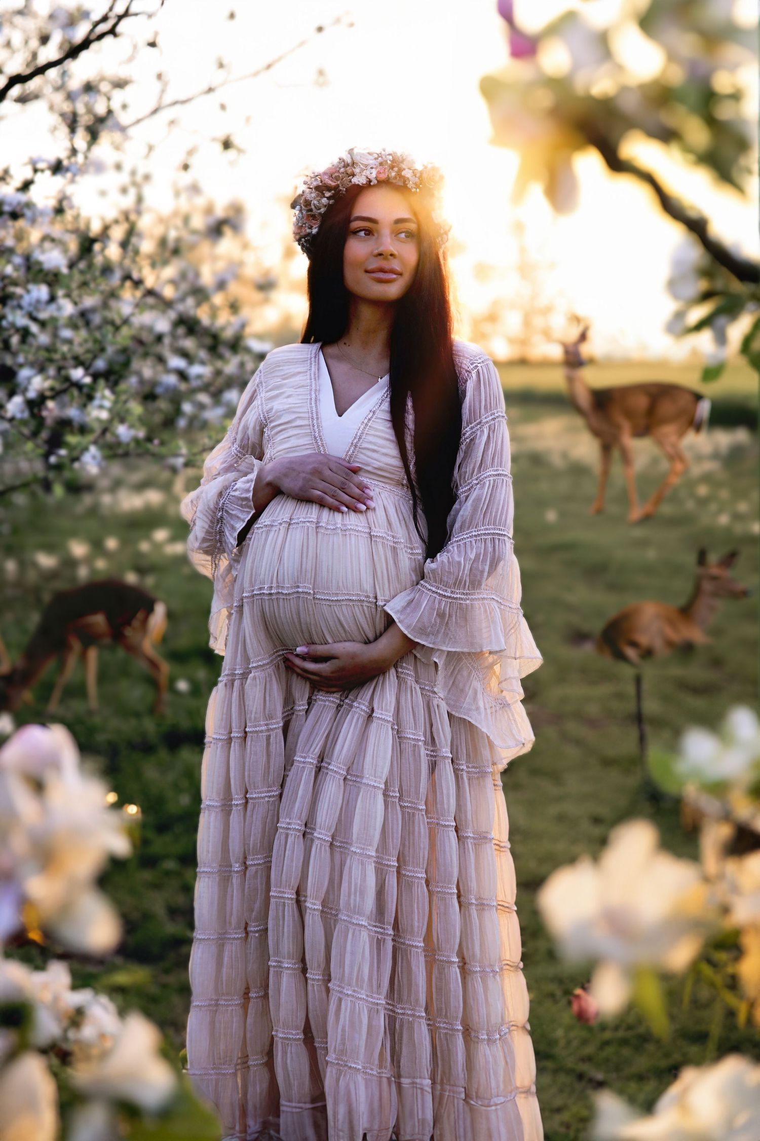 Ethereal maternity portrait in a flowing pink dress among blooming spring trees at sunset.