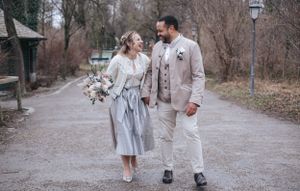 Hochzeitsfotografie: Brautpaar in Tracht geht gemeinsam über einen Weg im Grünen und blickt sich lächelnd an, aufgenommen im Raum Dachau.