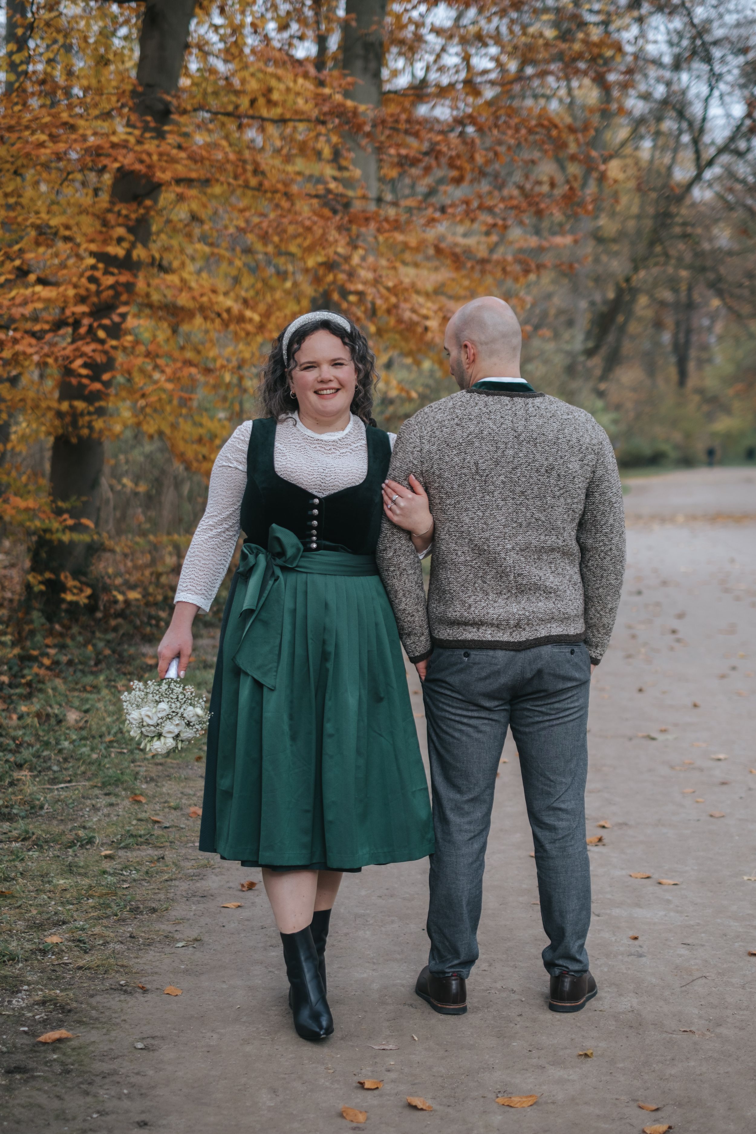 Hochzeitsfotografie München:: Brautpaar geht gemeinsam einen Weg durch einen herbstlichen Wald, aufgenommen von hinten.