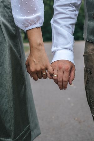 Hochzeitsfotografie: Detailaufnahme der Hände eines Brautpaares mit Eheringen, aufgenommen im Freien auf einem Weg.