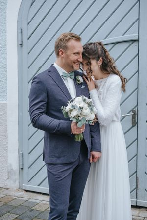Hochzeitsfotografie: Brautpaar steht eng beieinander vor einer hellen Tür, beide lächeln sich ruhig an.