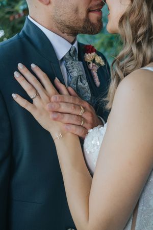 Hochzeit: Nahaufnahme eines Brautpaares: Die Braut legt ihre Hand mit Ehering auf die Brust des Bräutigams, beide stehen eng beieinander.