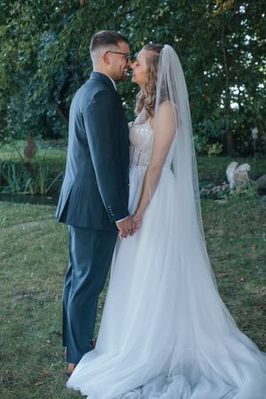 Hochzeitsfotografie: Brautpaar steht sich im Grünen gegenüber und hält sich an den Händen, beide tragen Hochzeitskleidung.