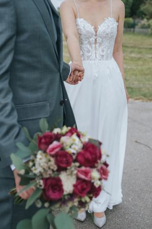 Hochzeitsfotografie: Braut und Bräutigam halten sich an den Händen, der Brautstrauß ist im Vordergrund sichtbar.
