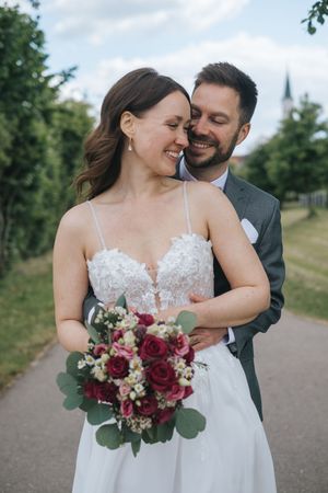 Hochzeitsfotografie: Brautpaar steht eng beieinander, die Braut hält einen Blumenstrauß, beide lächeln sich an.