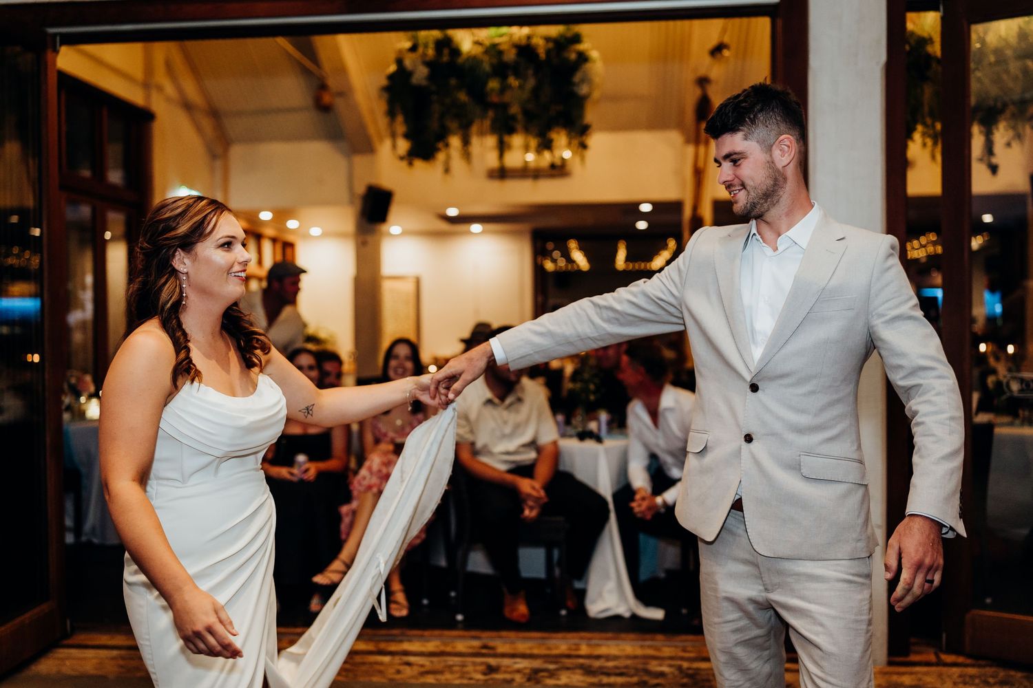 Newlyweds perform their first dance surrounded by guests in a warmly lit reception venue during their wedding celebration.