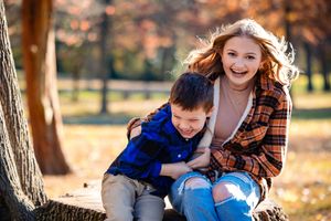 A couple shares joyful moments together in a park during autumn with golden leaves on the ground.