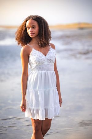 A white lace summer dress flows in the ocean breeze during a beachside photoshoot at sunset.