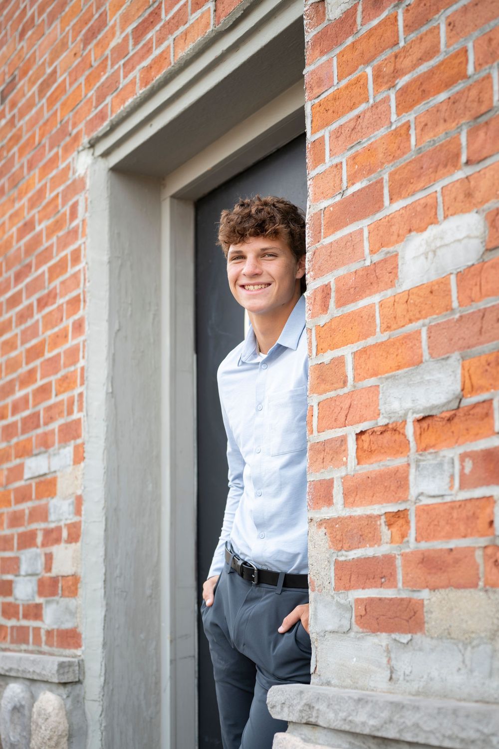 A person in light blue shirt peeks out from a brick doorway with a cheerful expression.
