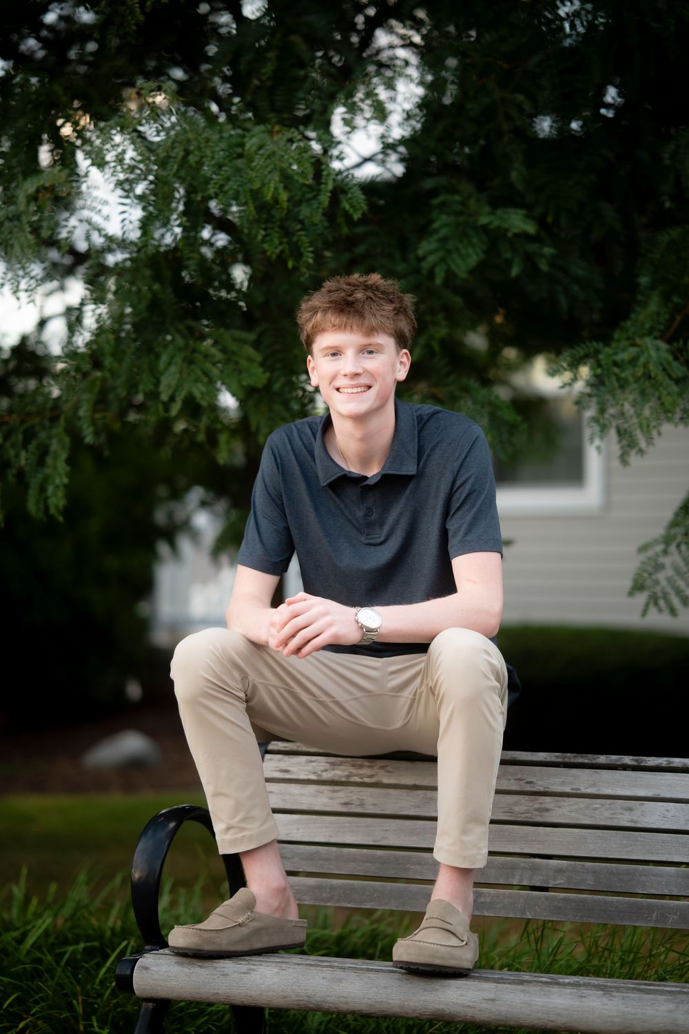 Casual outdoor portrait session on a wooden park bench surrounded by trees.
