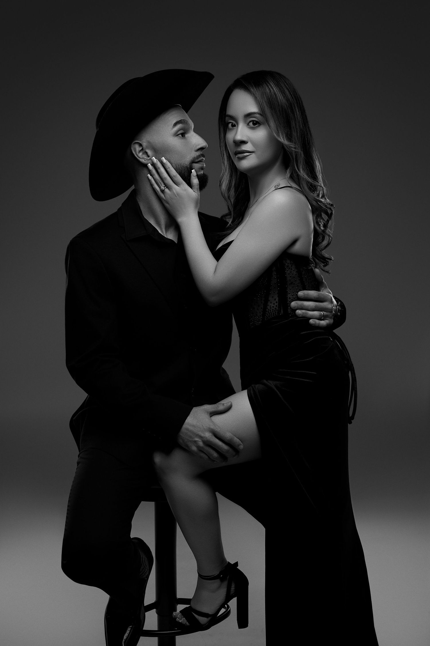 Black and white studio photo of an elegant couple posing intimately, woman in evening dress touching mans face.