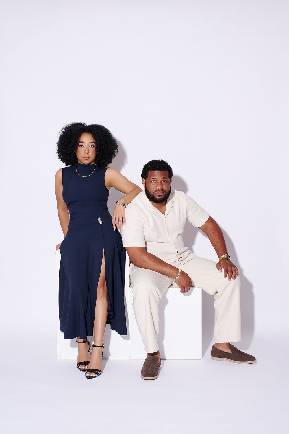 A woman in a navy dress and a man in cream outfit pose elegantly against a white studio background. NJ studio engagement