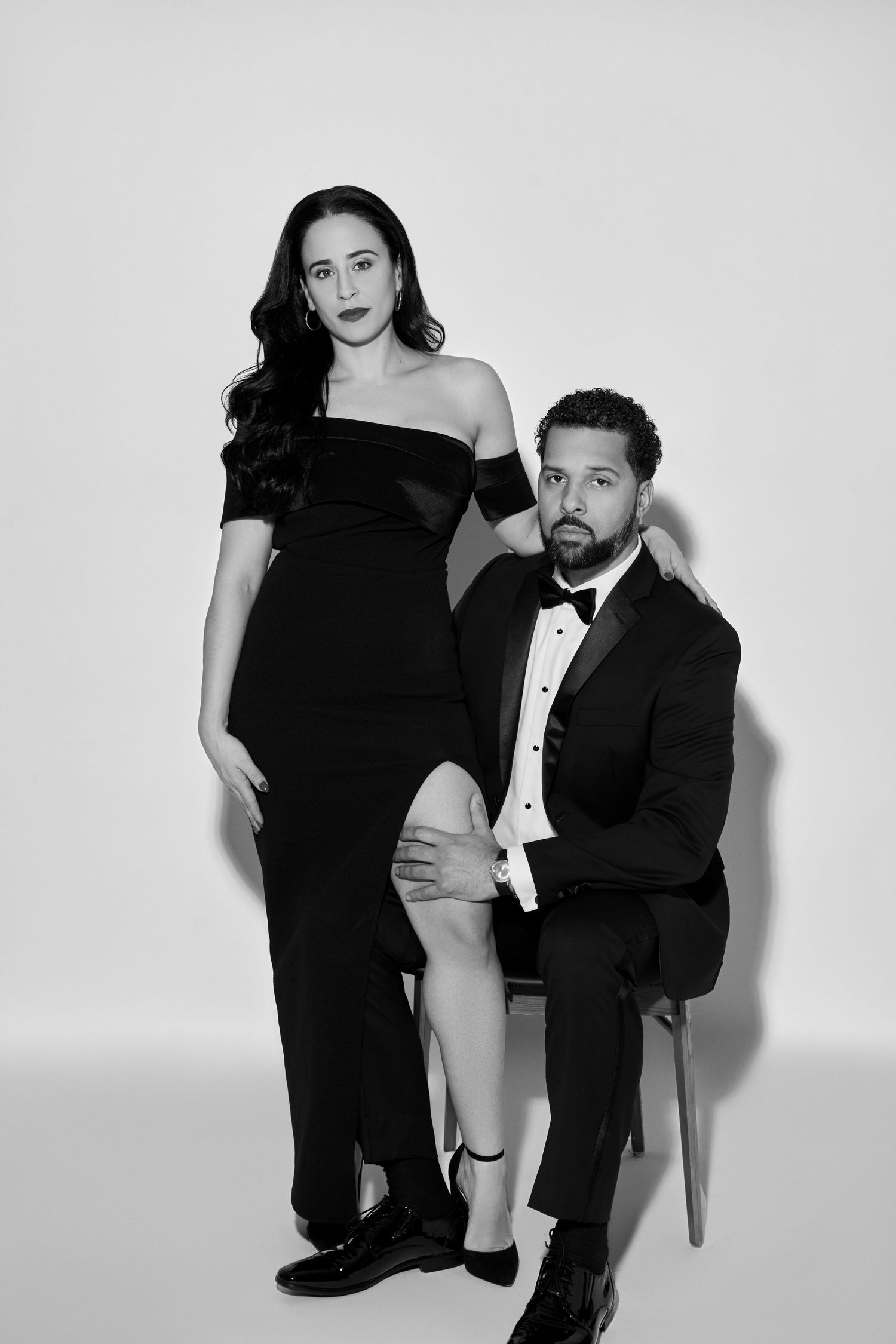 Black and white studio portrait of a couple in formal attire, with one person seated and one standing.
