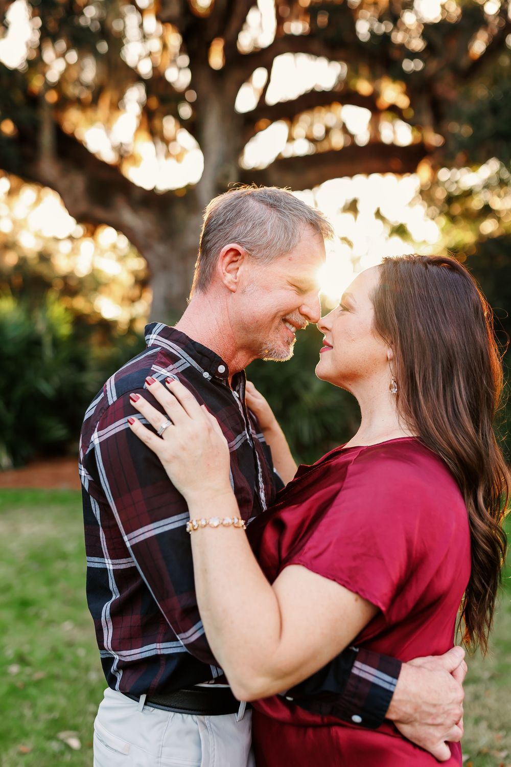 Romantic couple embraces outdoors at sunset with sunlight filtering through trees in background.