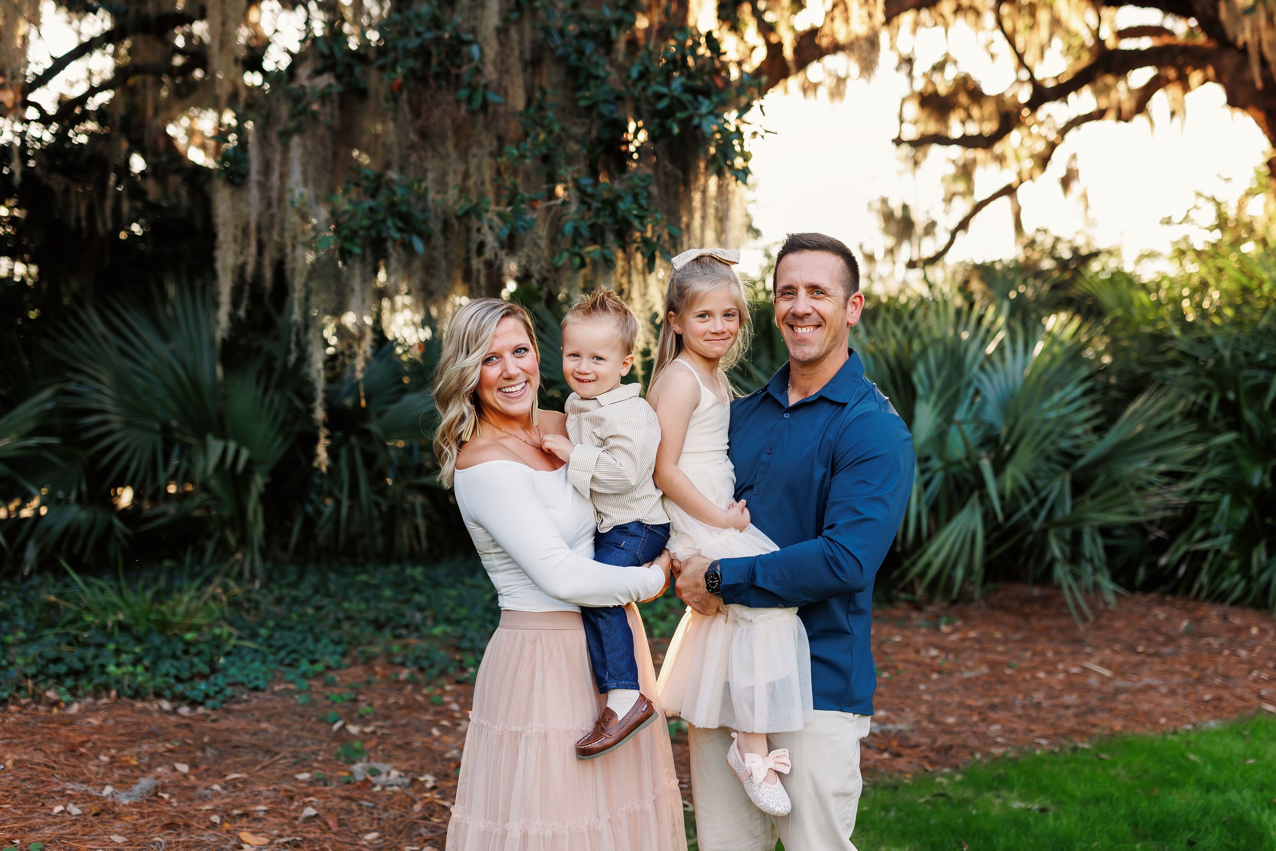 A family in coordinated pink and navy outfits poses together in a lush garden setting during golden hour.